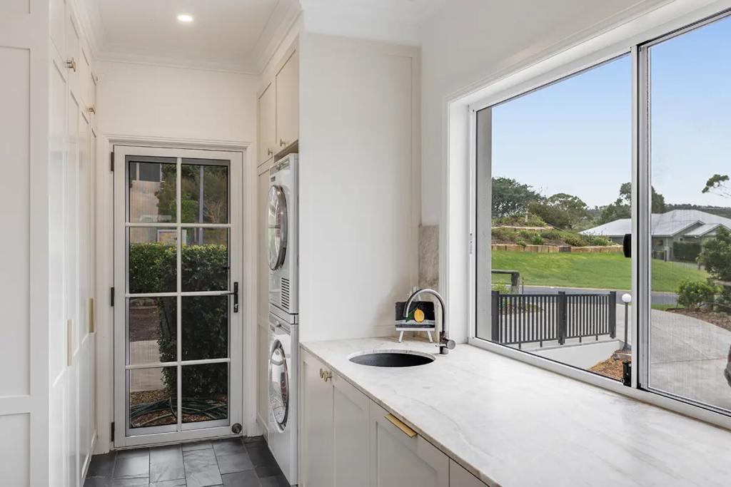 Hodgsonvale House Renovation (A bright laundry room with white cabinets, stacked washer/dryer, and a large window.)