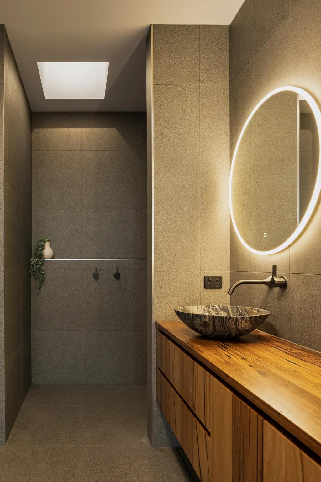 Project Treevue (A modern bathroom with grey tiled walls, and a large round mirror with LED lighting)