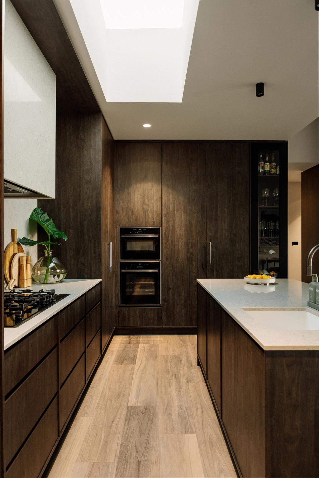 Lavish Morada (Contemporary kitchen with dark wood cabinets, skylight, built-in ovens, and island sink.)