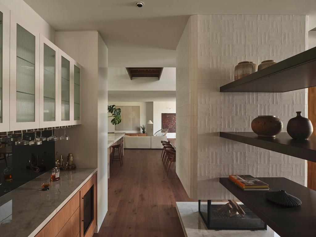 Project Riverton (View from a wet bar down a hallway toward a living area, featuring textured tile and shelving.)