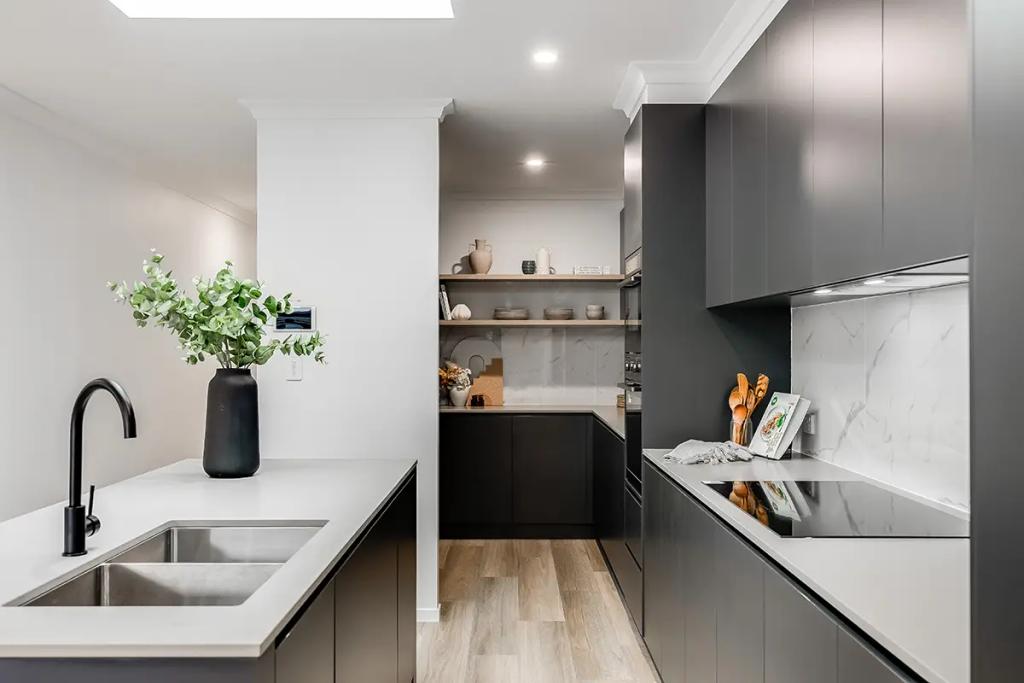 Modern kitchen with dark gray cabinets, white marble backsplash, stainless steel sink and faucet, and wooden flooring