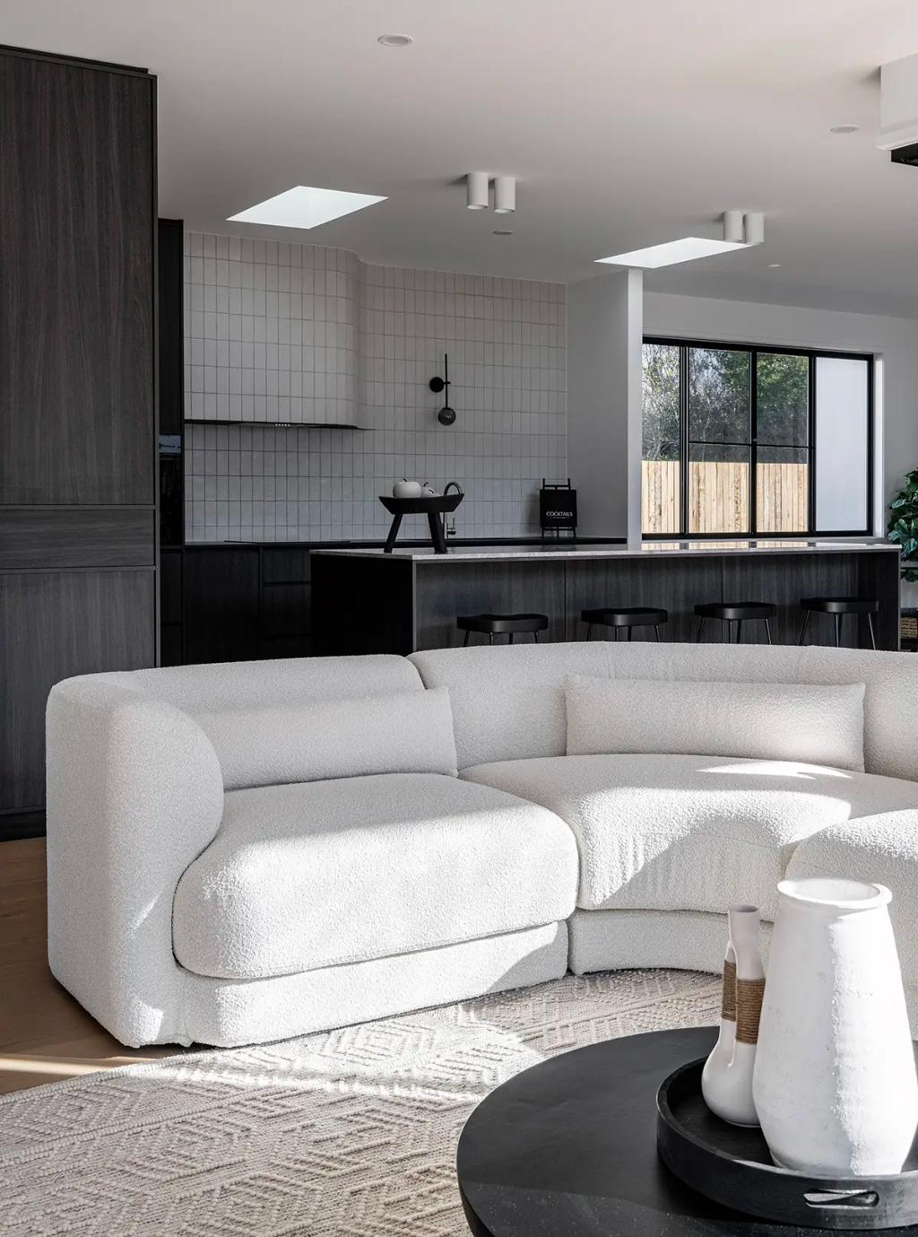 Project Ward 2.0 (A modern living space featuring a cozy white boucle sofa, a minimalist black kitchen with dark cabinetry, and soft natural light filtering through large windows)