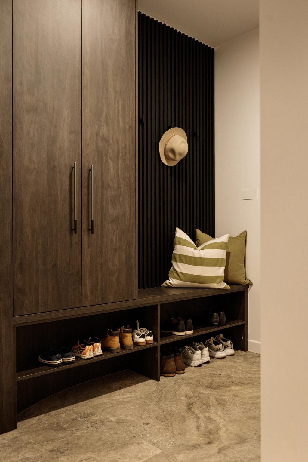 Lavish Morada (Mudroom with dark wood storage, cushioned bench, striped pillow, and organized shoe shelves.)