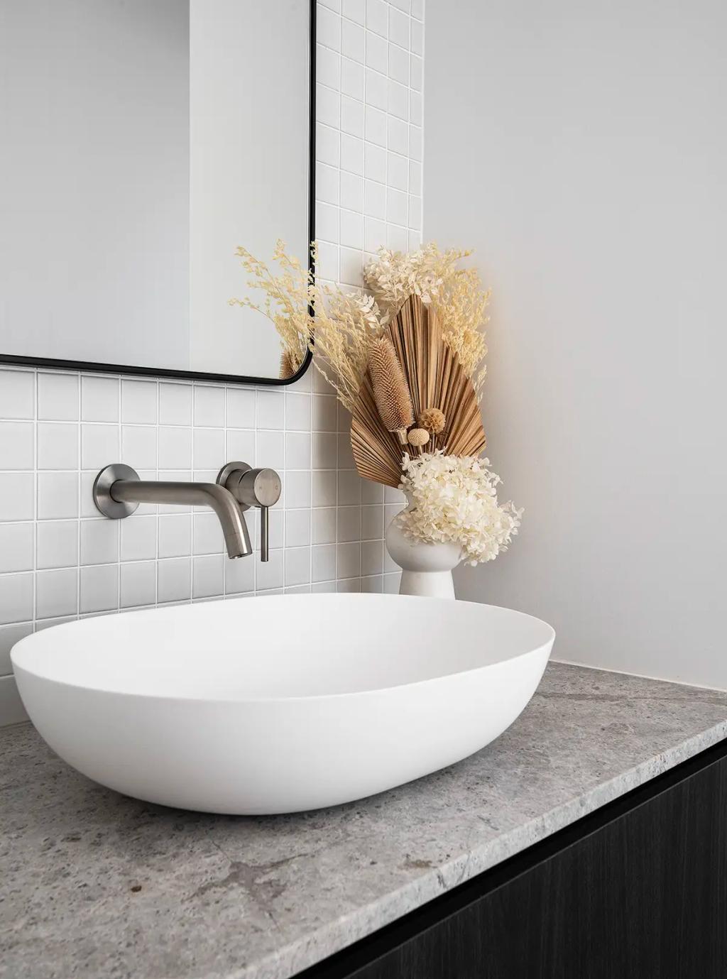 Project Ward 2.0 (A modern bathroom vanity with a white vessel sink, a gray stone countertop, white tiles, and dried floral decor)