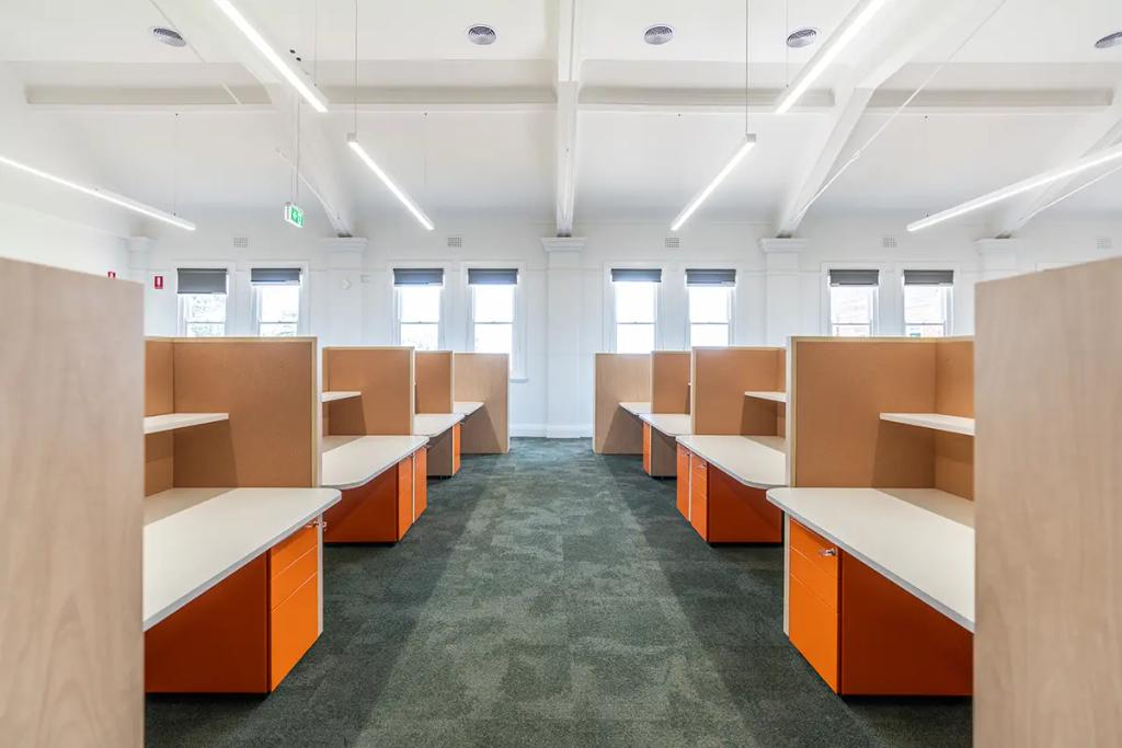 Downlands College Toowoomba Refurbishment (Bright office with rows of wooden cubicles, orange drawers, and large windows letting in daylight.)