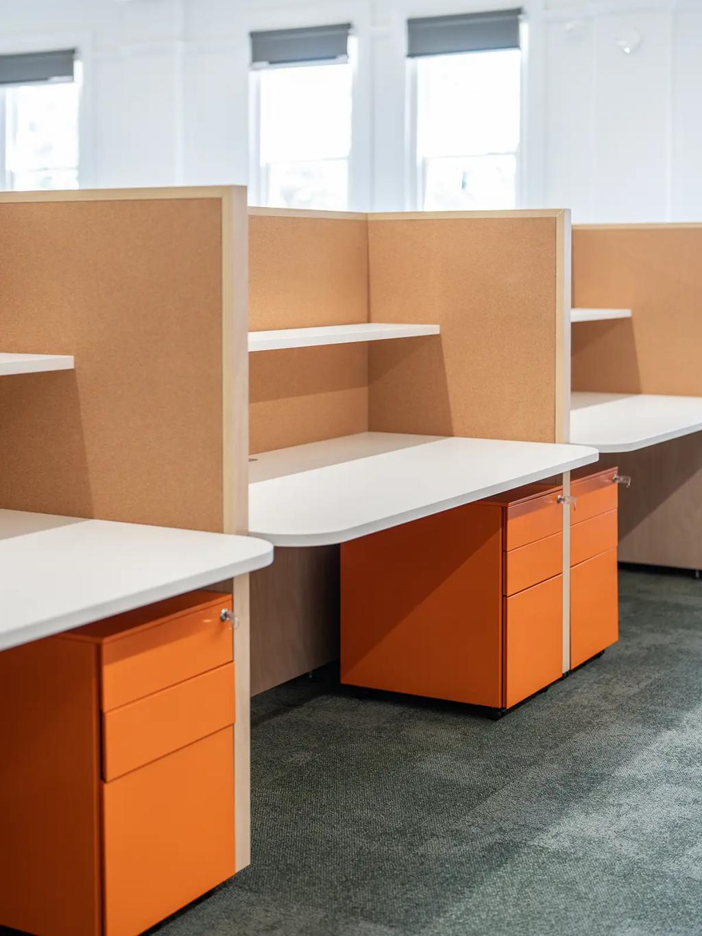 Downlands College Toowoomba Refurbishment (Close-up of modern office cubicles with white desks, corkboard dividers, and bright orange drawer units.)