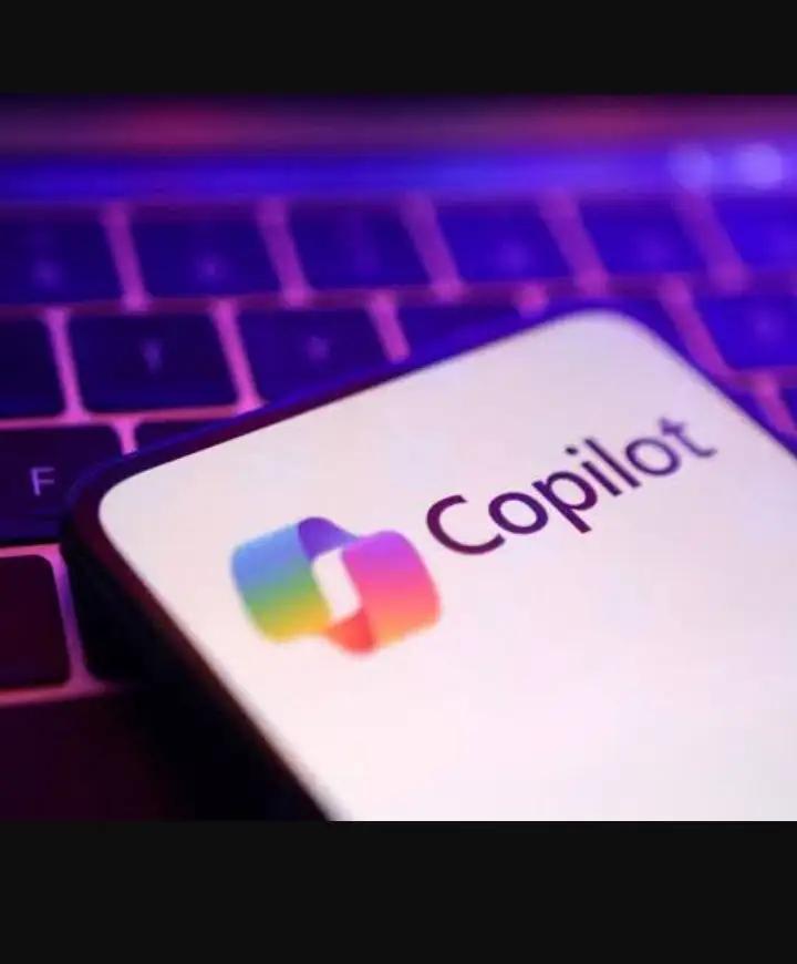 A close-up shot of a smartphone screen displaying the colorful Microsoft Copilot logo and text on a clean white background. The phone is placed over a laptop keyboard with vibrant purple and magenta backlighting, representing the integration of GPT-5.3 AI into the Microsoft 365 ecosystem
