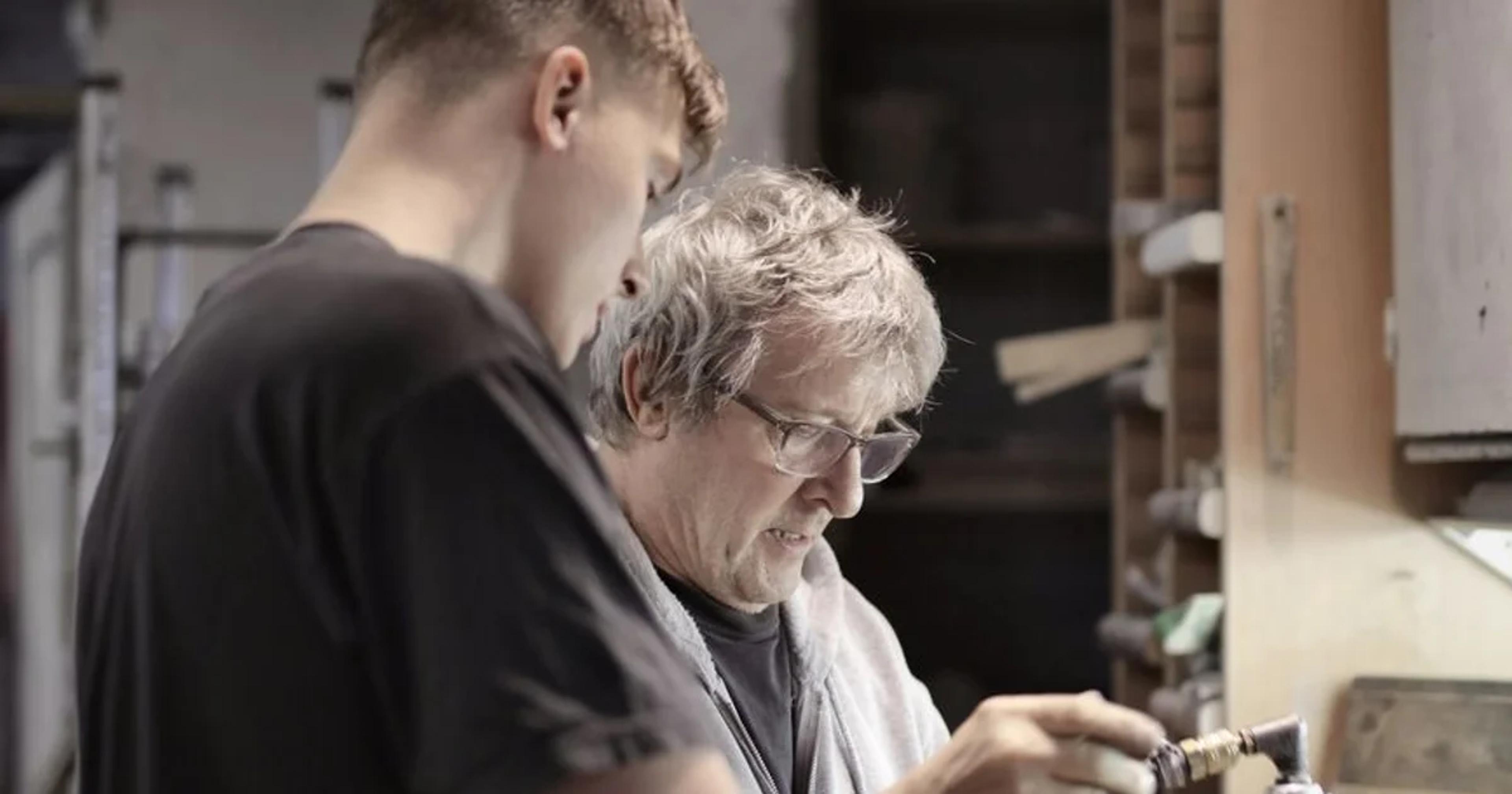 An elderly mentor and a young professional working together on a futuristic digital interface representing shared knowledge.