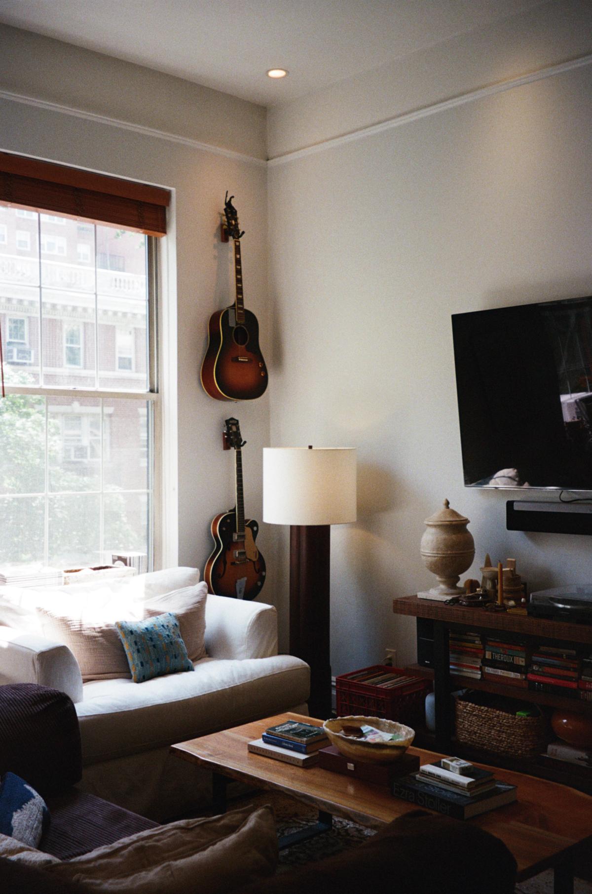 Ellie and Dan's apartment interior with cozy white chair, warm wood accents, lamp, and guitars.