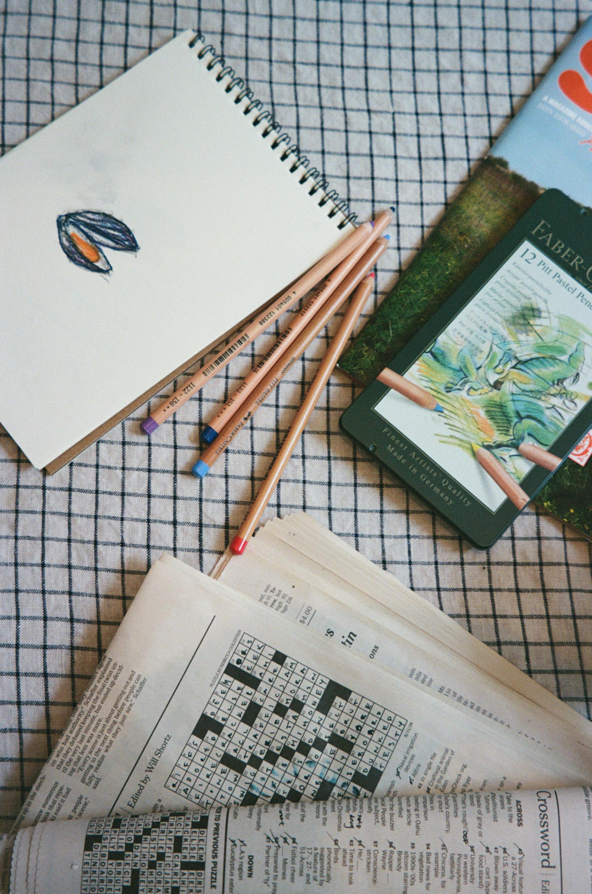 Plaid tablecloth featuring crosswords, colored pencils, and hand drawing of a clam..