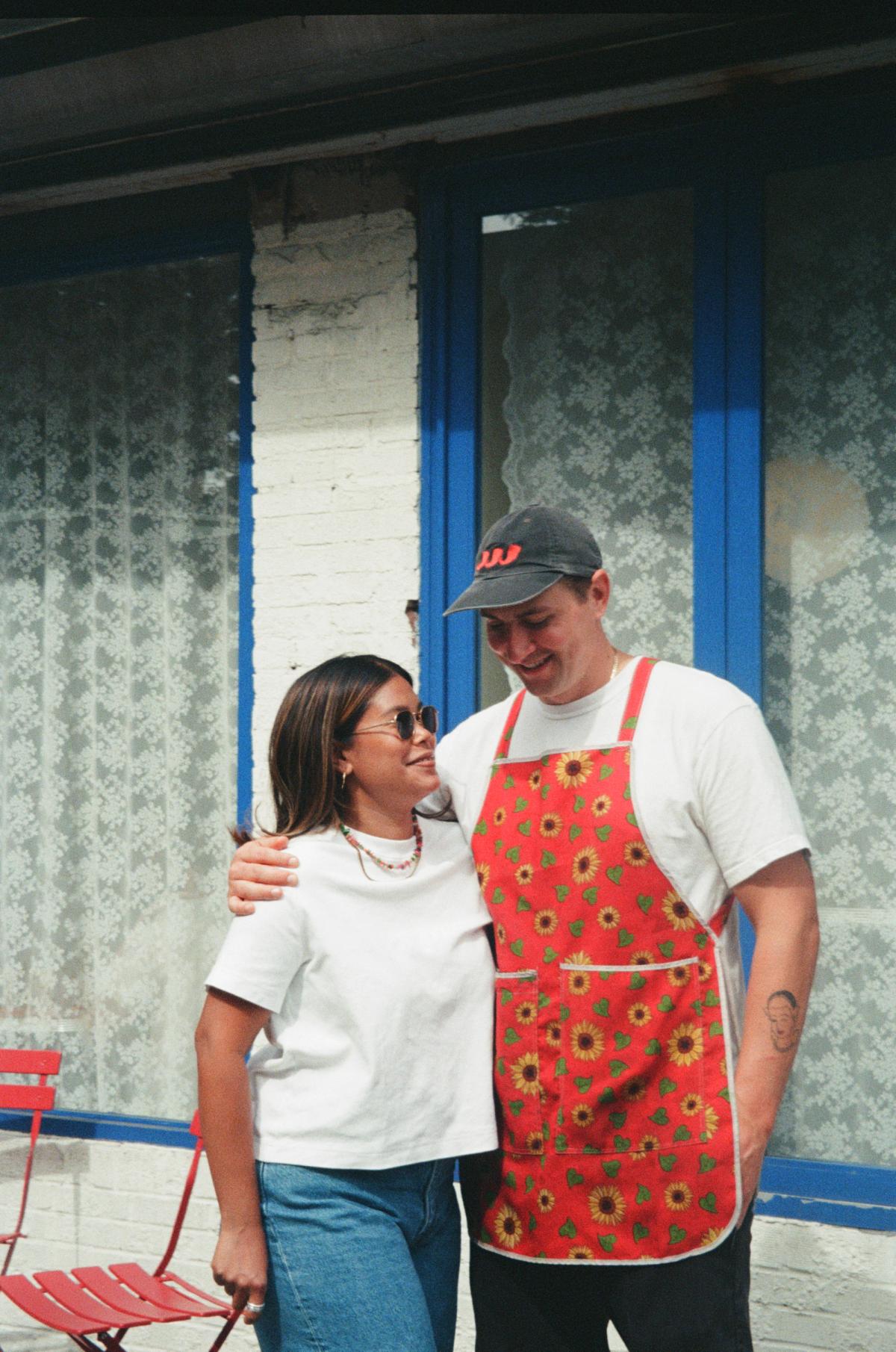 Trevor and Pias smile at eachother in front of their restaurant.