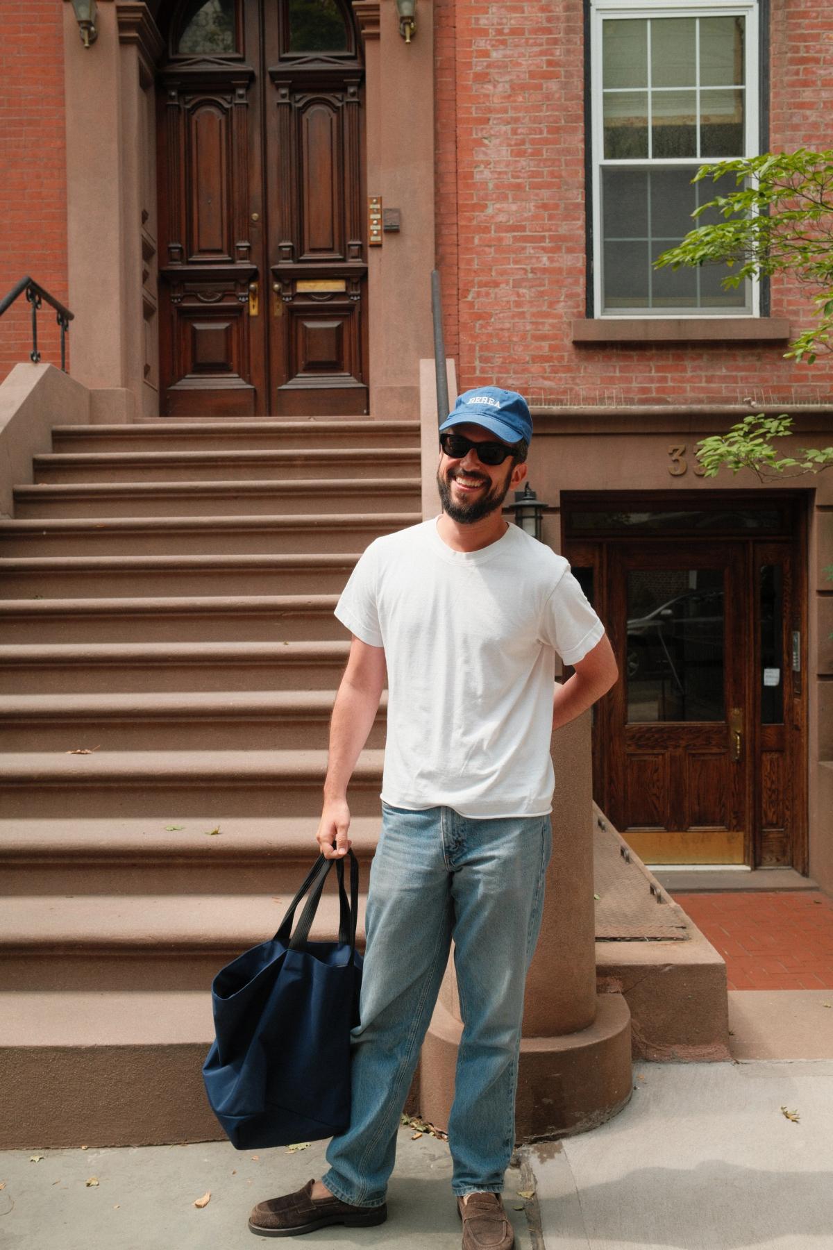 Dan styled in jeans, white tee, baseball cap, and French shopping bag.