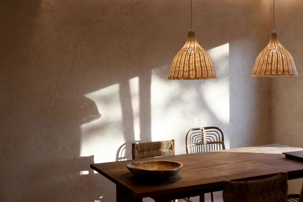 A warm rattan pendant light casting a soft pool of light over a worn timber surface and handthrown ceramic collection