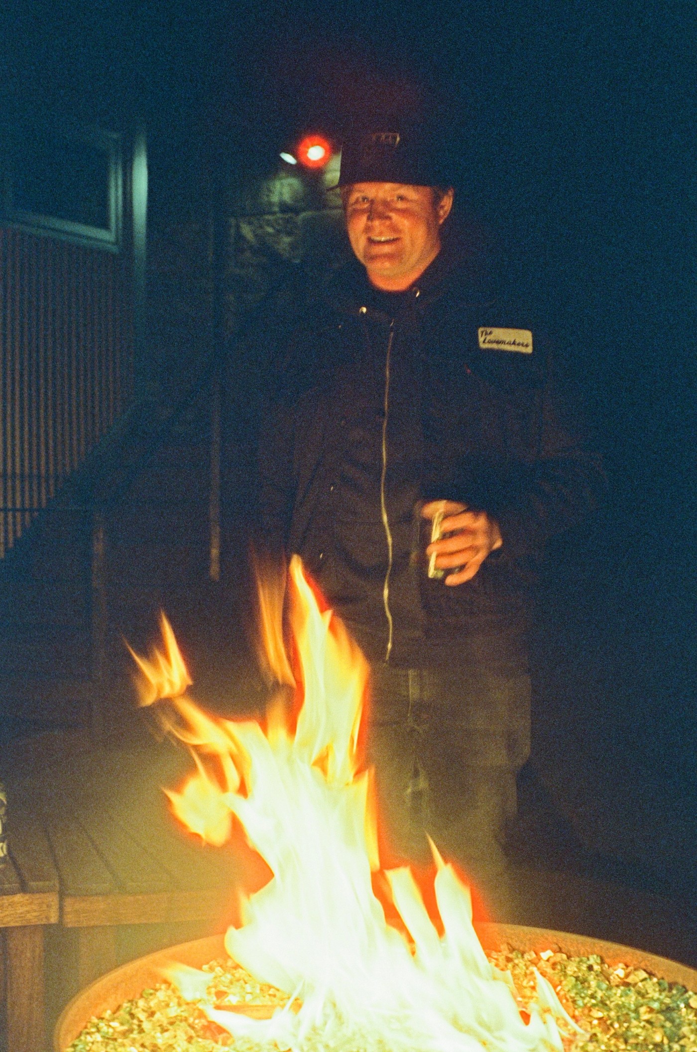 a man standing behind a fire with a patch on his jacket