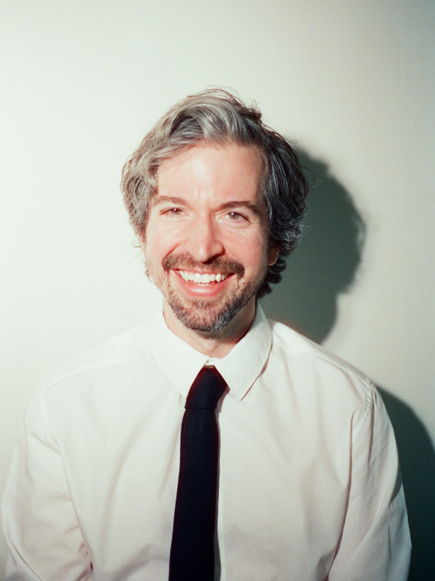 Eric Fenny, a man with gray hair and a beard wears a white shirt and black tie