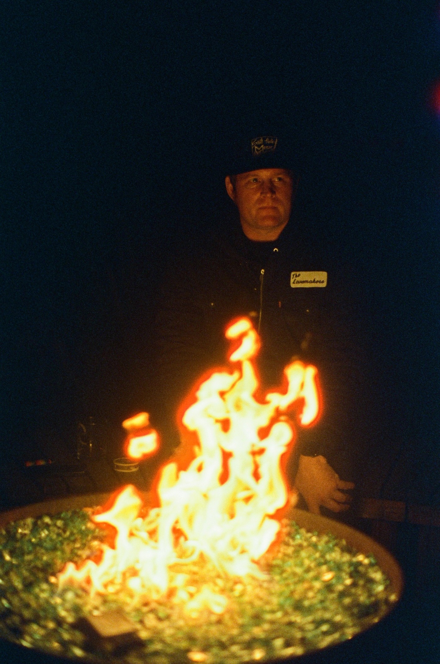 a man with a name tag that says the lovemakers sits behind a fire