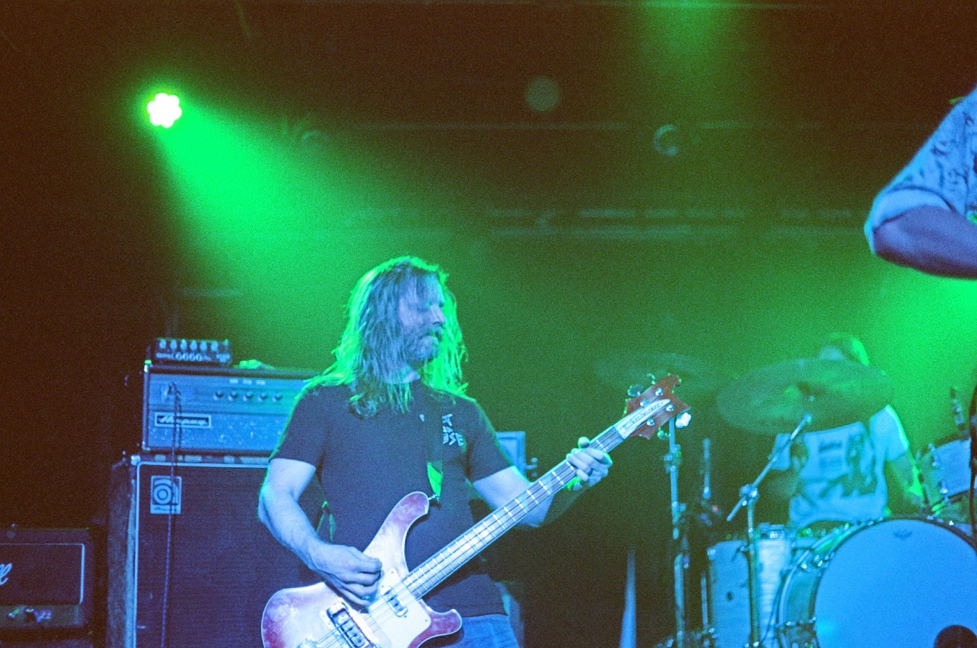 a man is playing a bass guitar on a stage in front of a drum set .