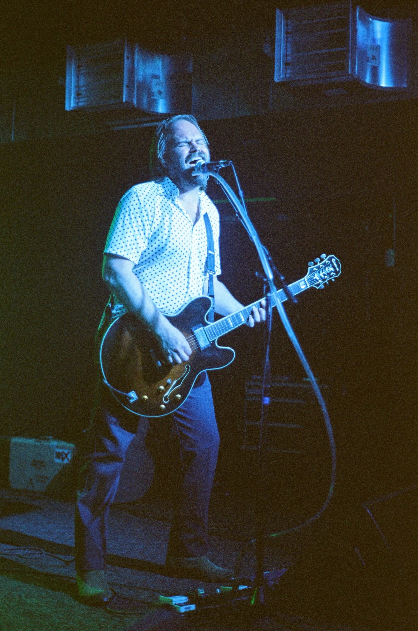 a man singing into a microphone while playing an epiphone guitar.