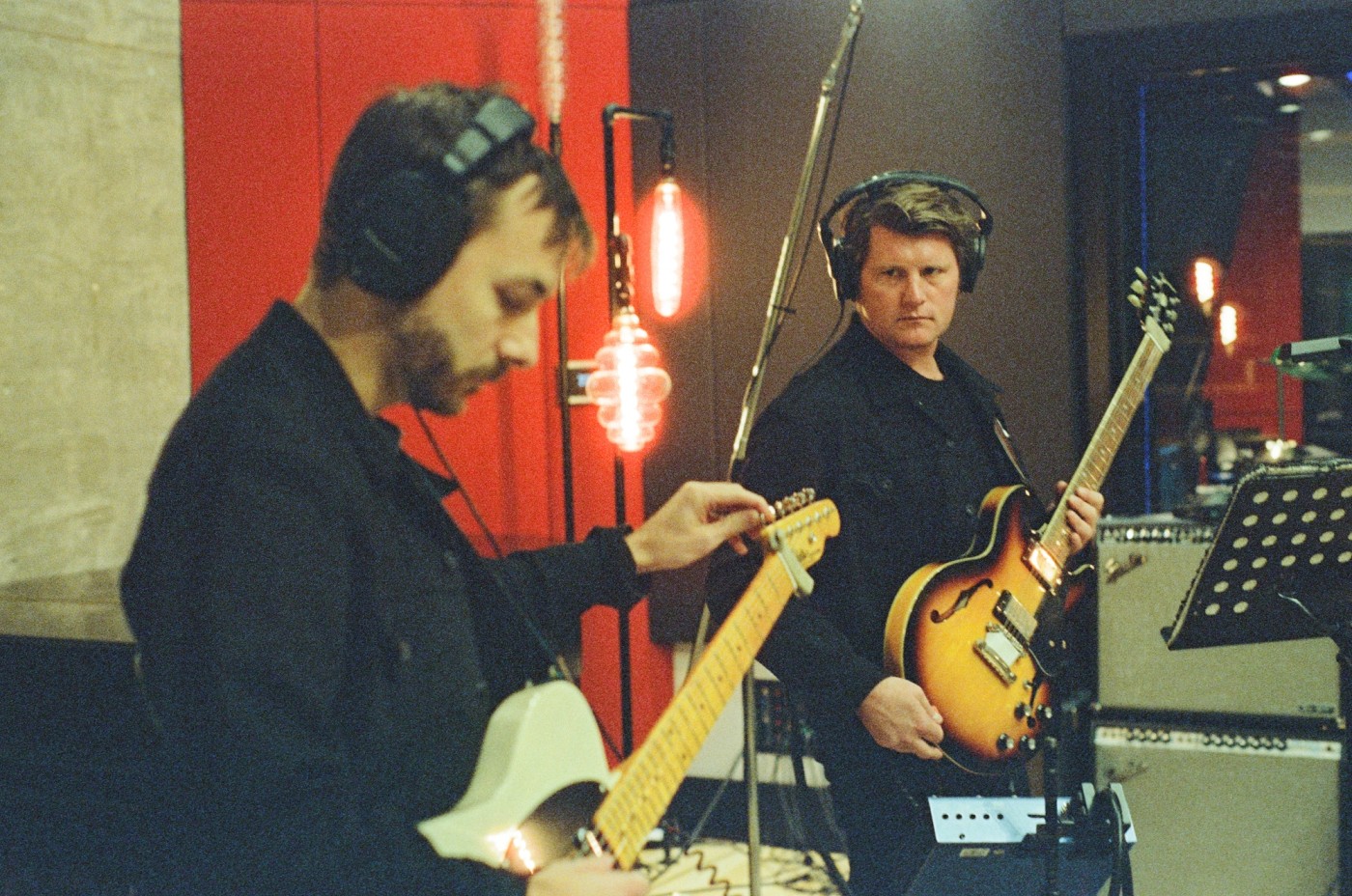 two men are playing guitars in a recording studio .