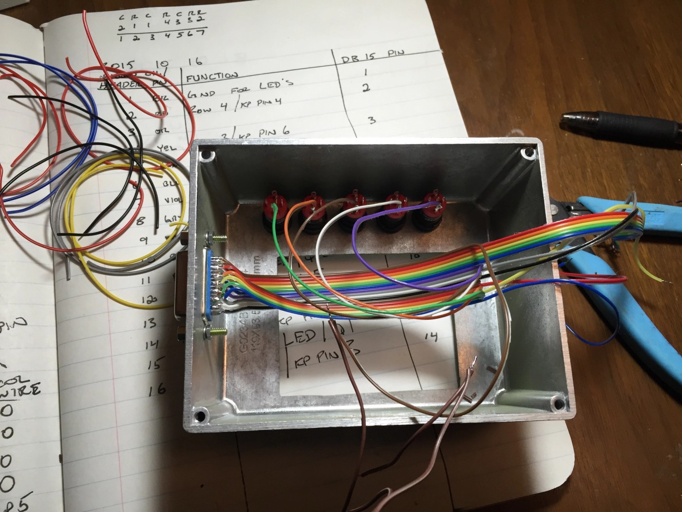 a box filled with wires is sitting on top of a wooden table next to a notebook .