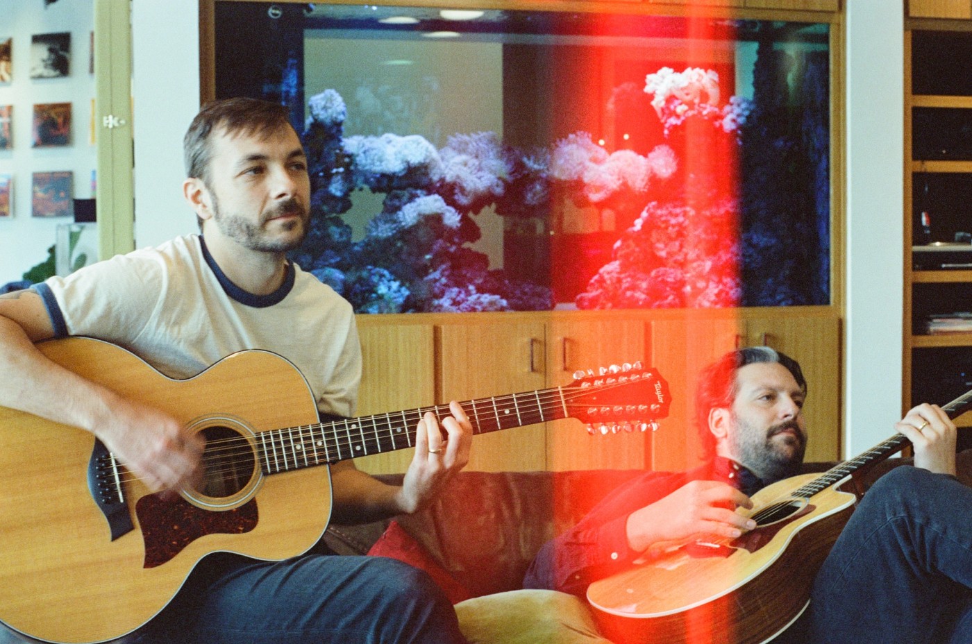 two men are playing guitars in a living room in front of an aquarium .