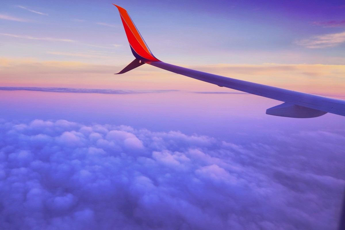 the wing of an airplane is flying over the clouds at sunset .