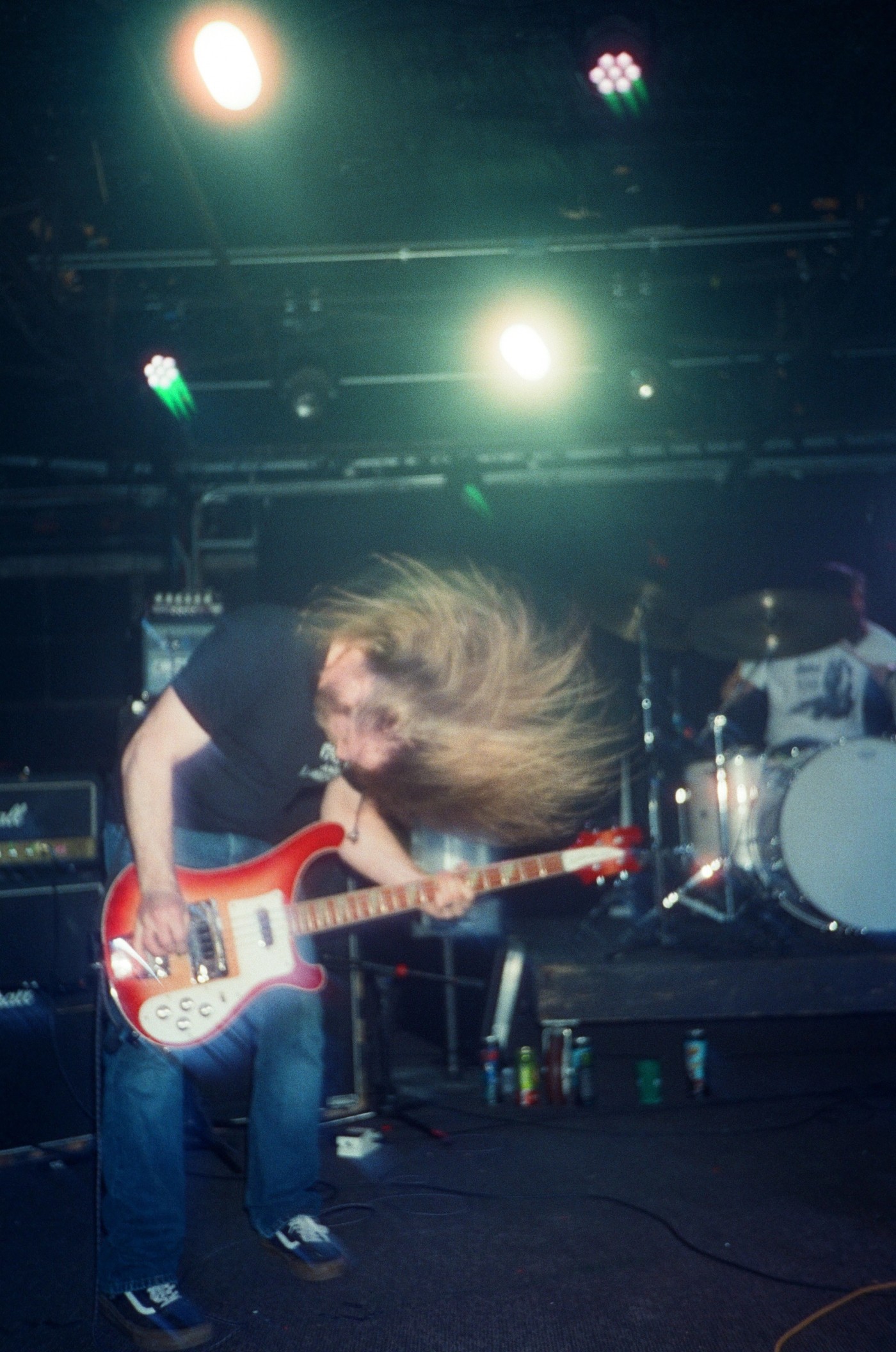 a man with long hair is playing a red bass guitar