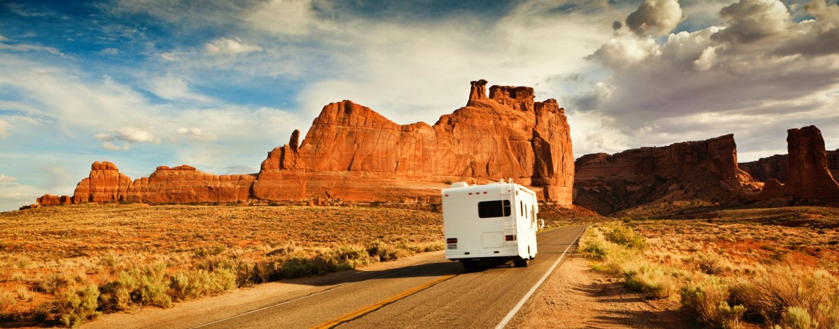 A white rv is driving down a desert road.