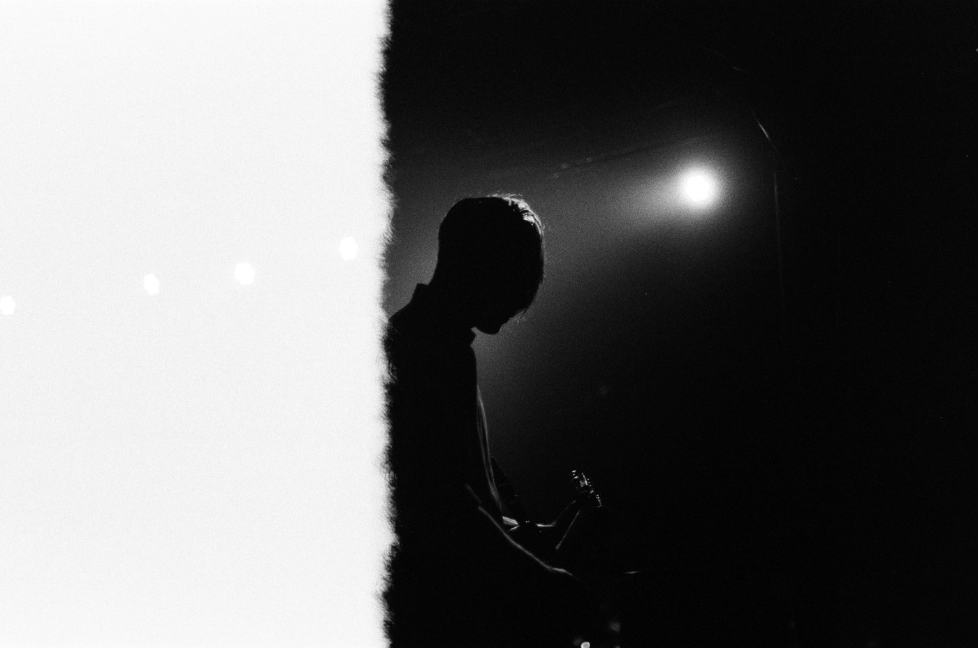 a black and white photo of a man playing a guitar in the dark .