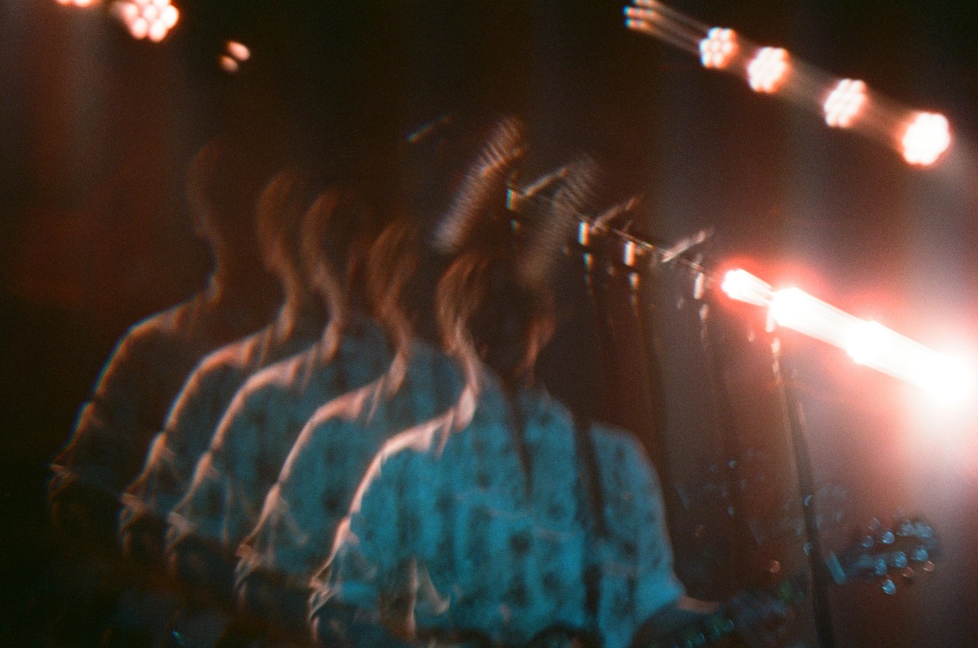 a blurry picture of a person playing a guitar and singing into a microphone on a stage .