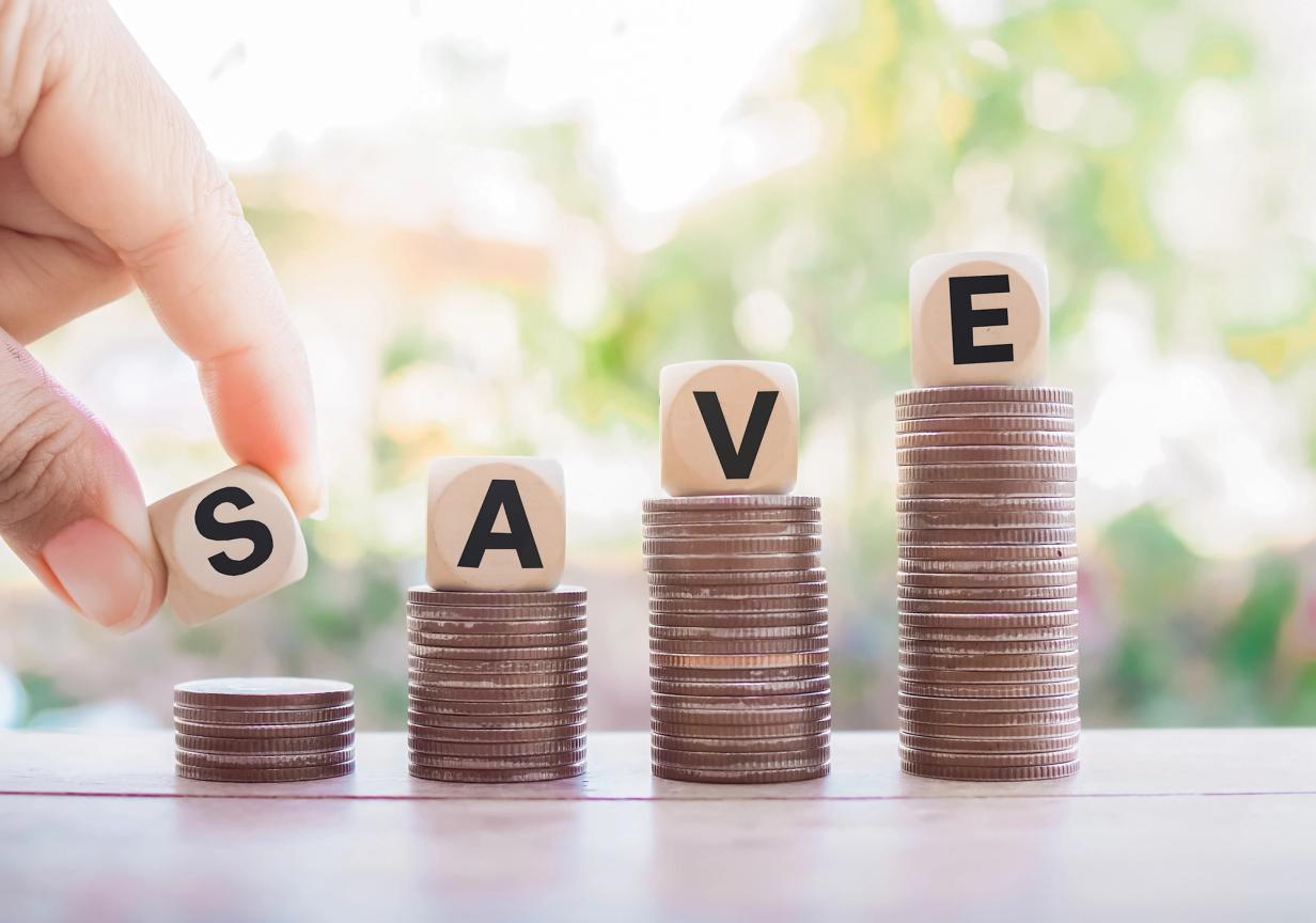 Coins stacked with dice spelling SAVE, symbolizing smart car-buying savings and money-saving tips.