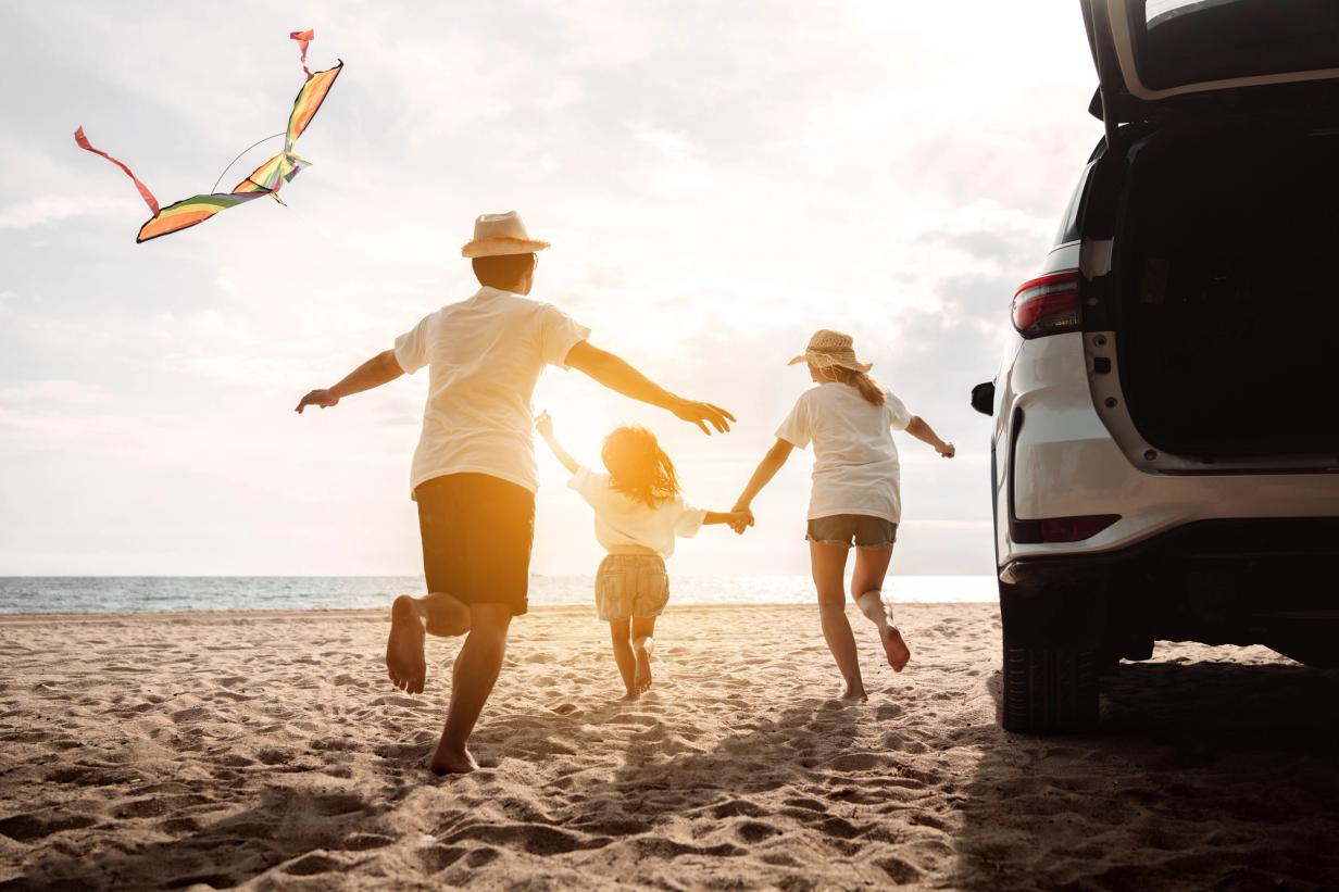 Family running on the beach near their parked car on a sunny day.