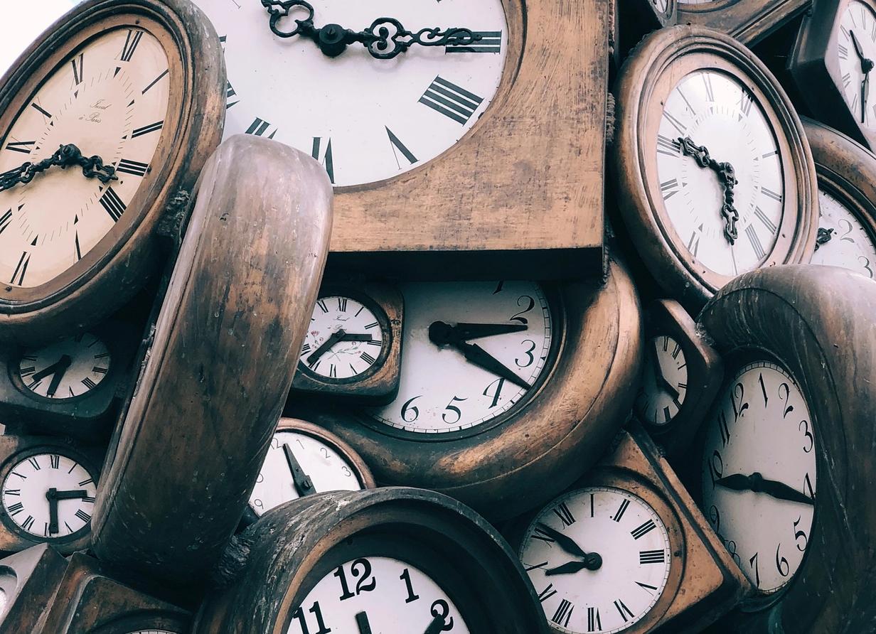 Pile of overlapping antique clocks with different times displayed.