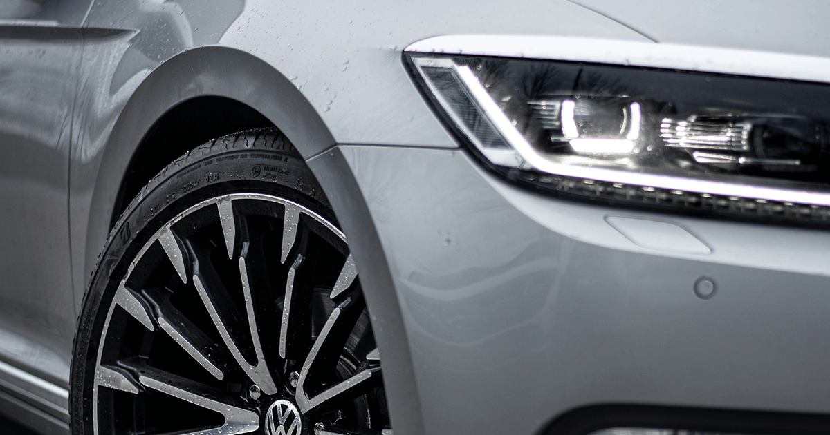 Close up of a car front wheel and headlight with raindrops on the body.