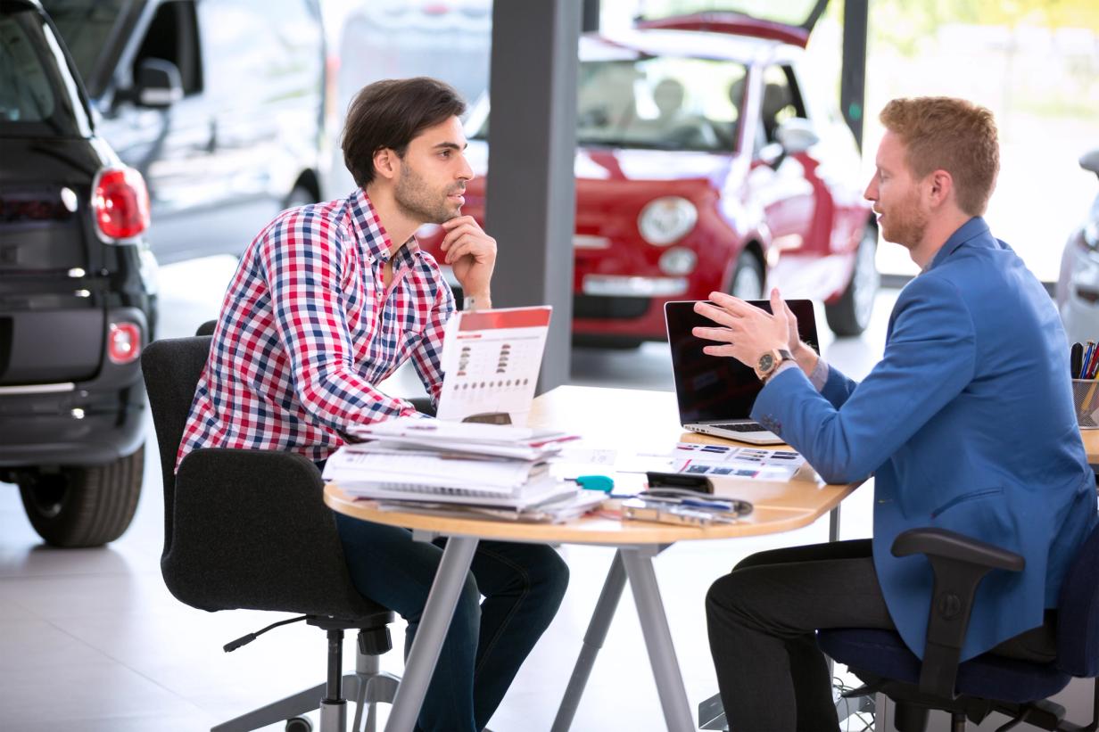 Two people sitting in a dealership discussing important questions to ask before buying a car and preparing for a confident purchase.