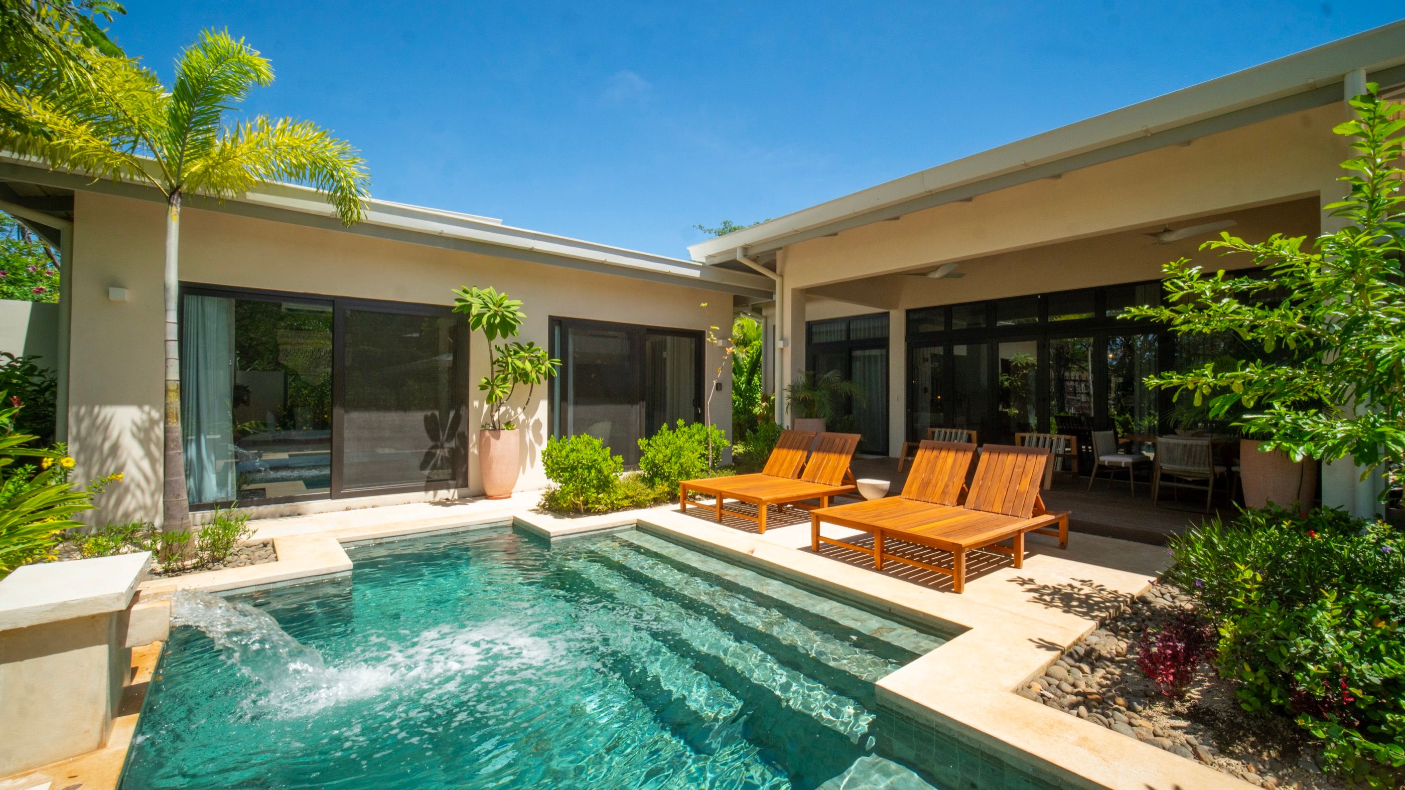 Single-storey home with a turquoise pool, teak loungers and palms under a clear sky