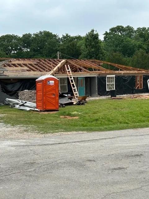 Single-story home with its roof torn off and a portable toilet in the yard at the start of a remodel