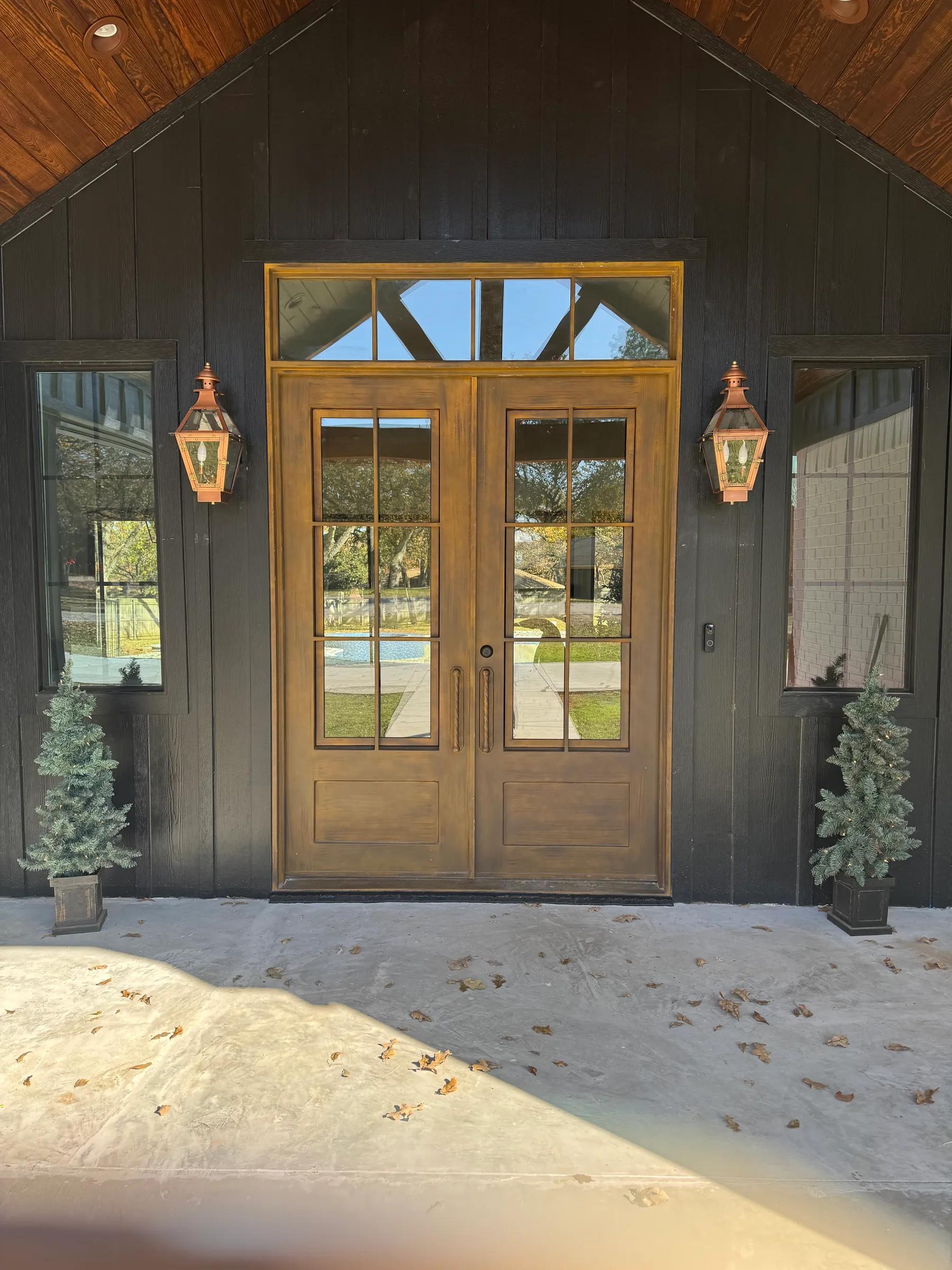 Arched wood double front doors with copper lanterns under a dark board-and-batten gable