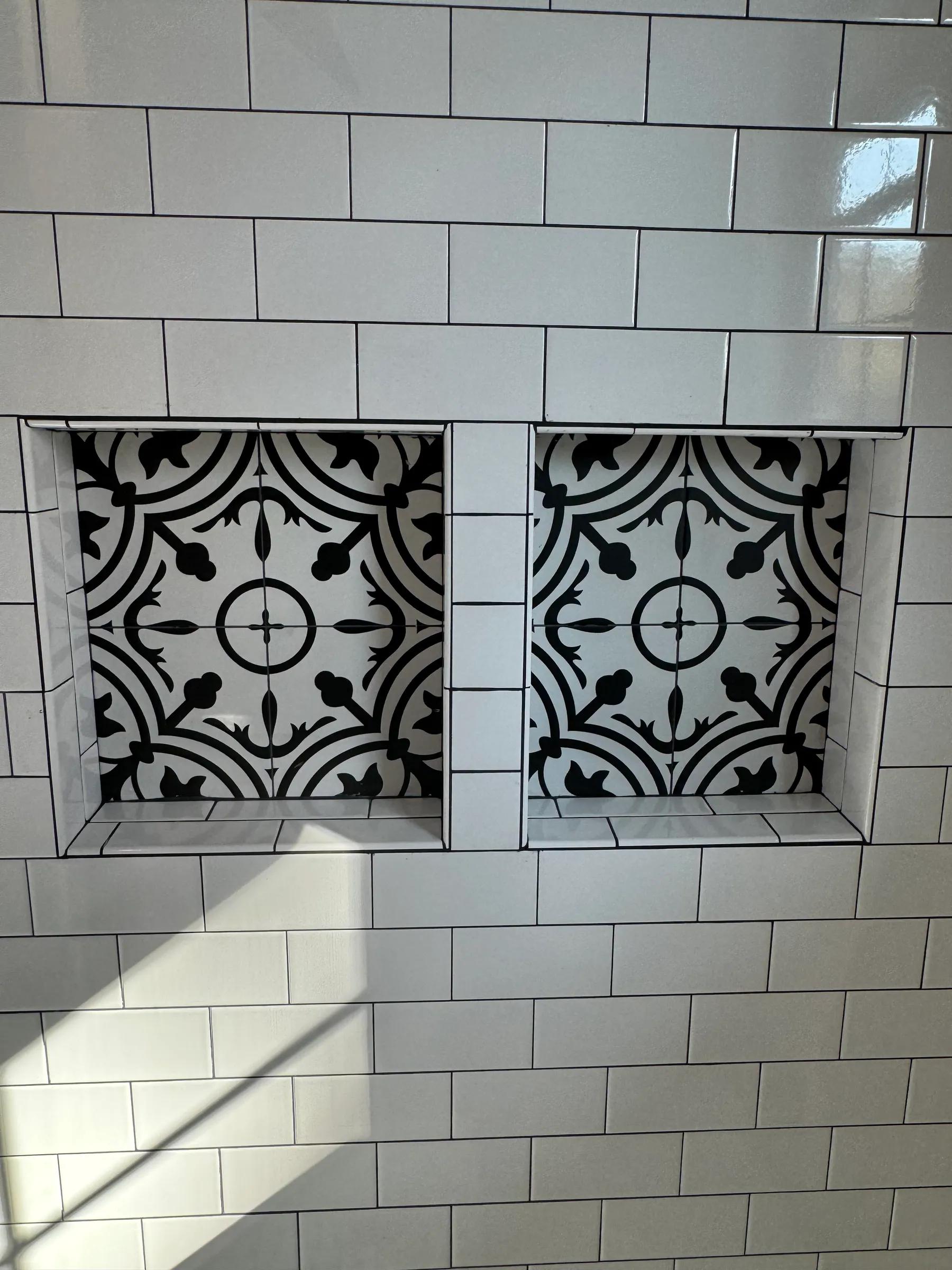 White subway tile shower with two niches lined in black and white patterned tile