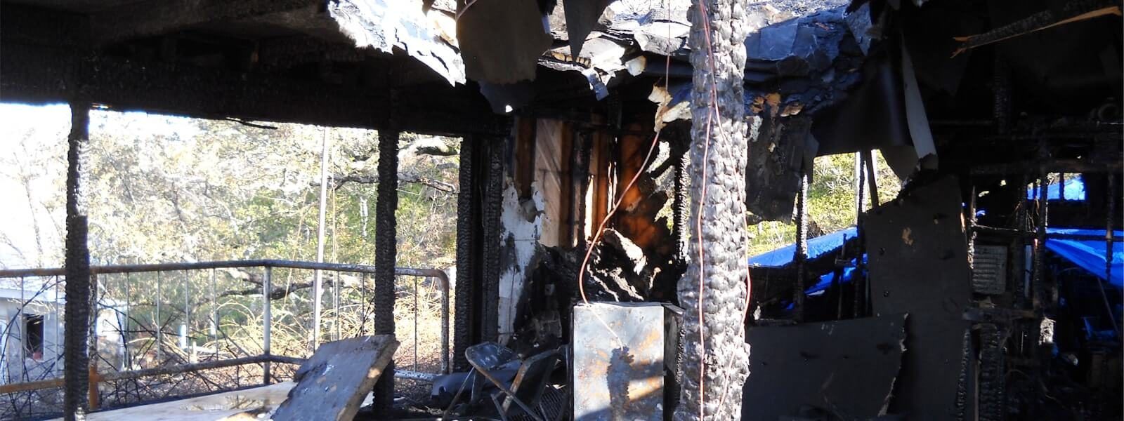 Fire-damaged great room with burned framing and debris before the rebuild