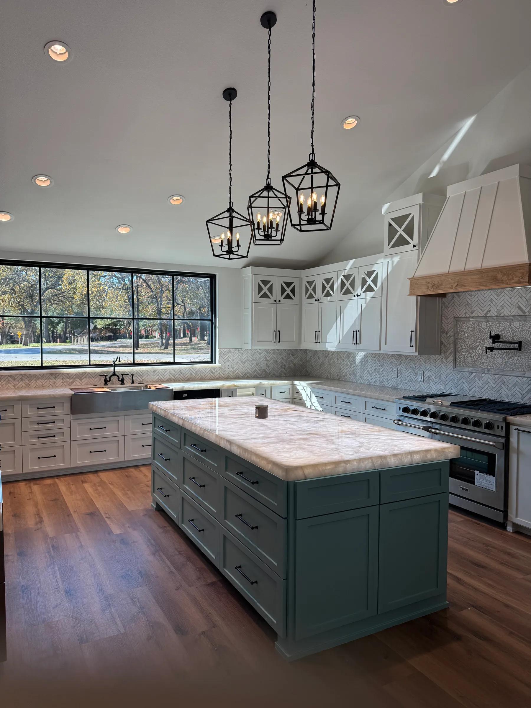 Open kitchen with a blue-green island, white cabinetry, and a wide black-framed window
