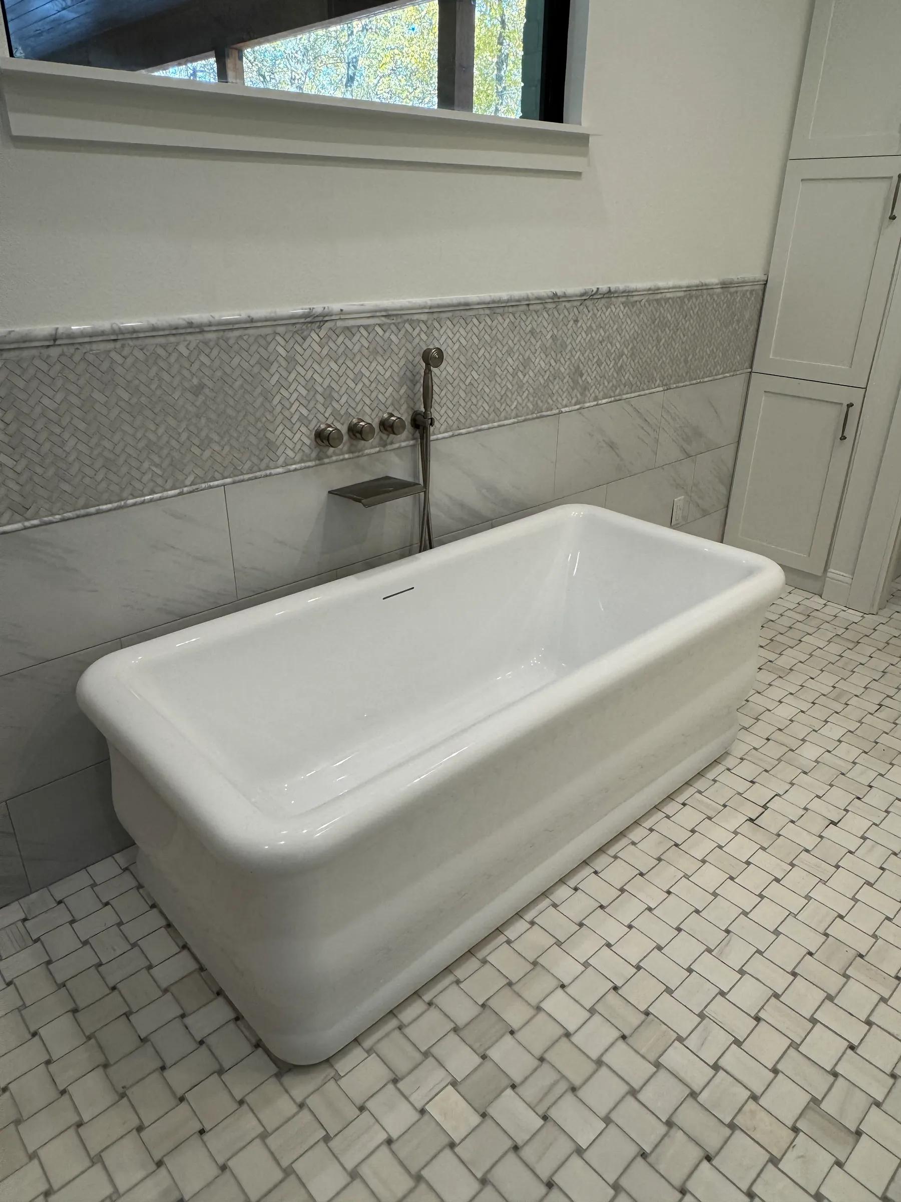 Freestanding soaking tub on a basketweave tile floor with a wall-mounted tub filler