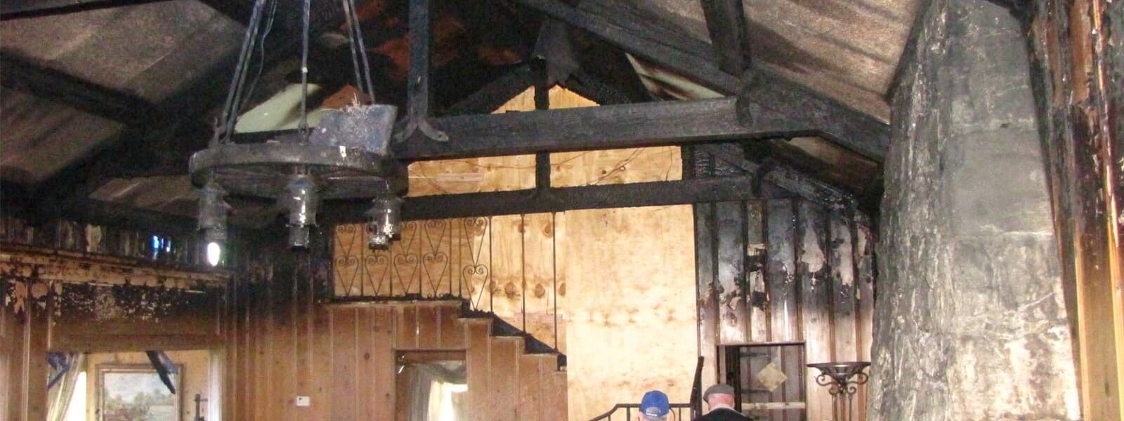 Great room after a house fire, with charred ceiling beams and smoke-blackened paneling