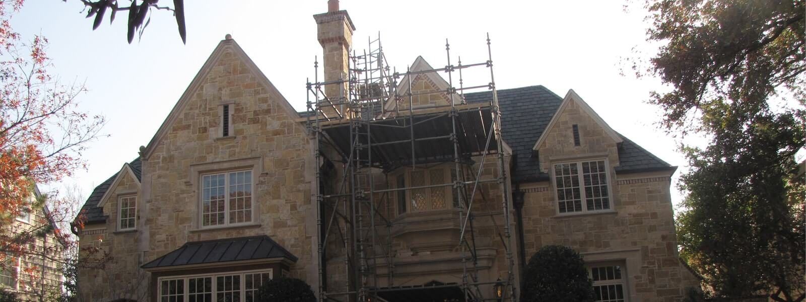 Two-story stone home with scaffolding during exterior repairs