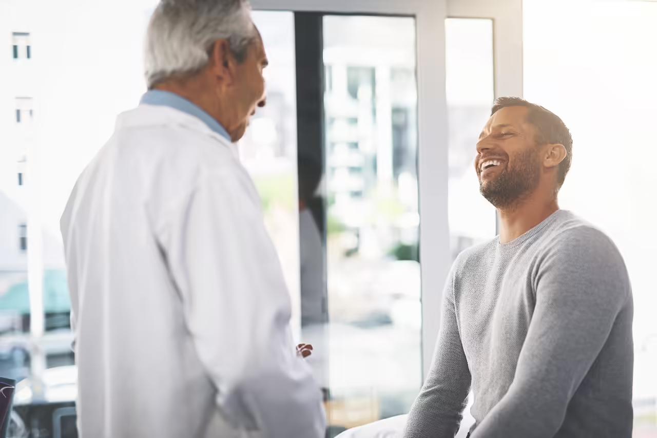 A smiling patient in a grey jumper talking with a consultant in a white coat in a bright, sunlit consulting room