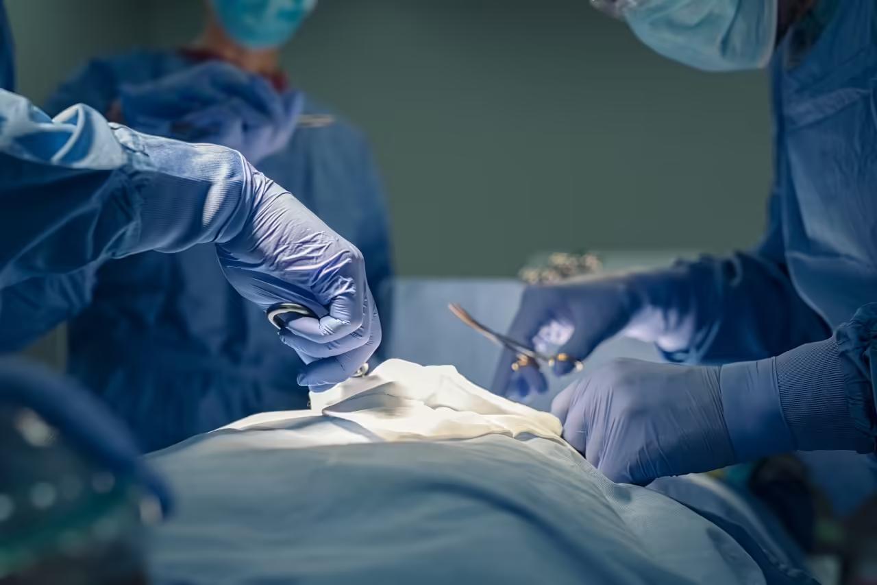 A surgical team in gowns, masks and gloves operating on a draped patient in theatre