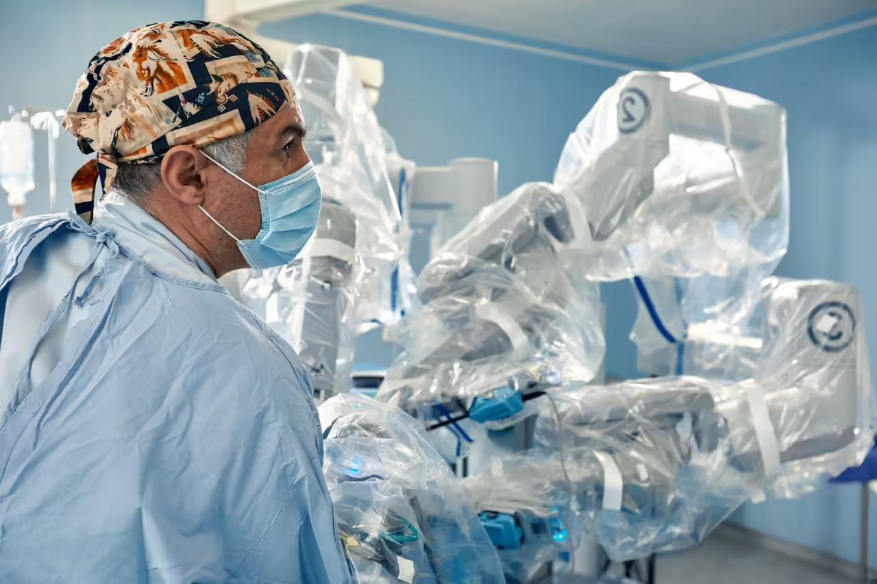A robotic surgical system positioned beside an operating table, with a gowned theatre team working behind it