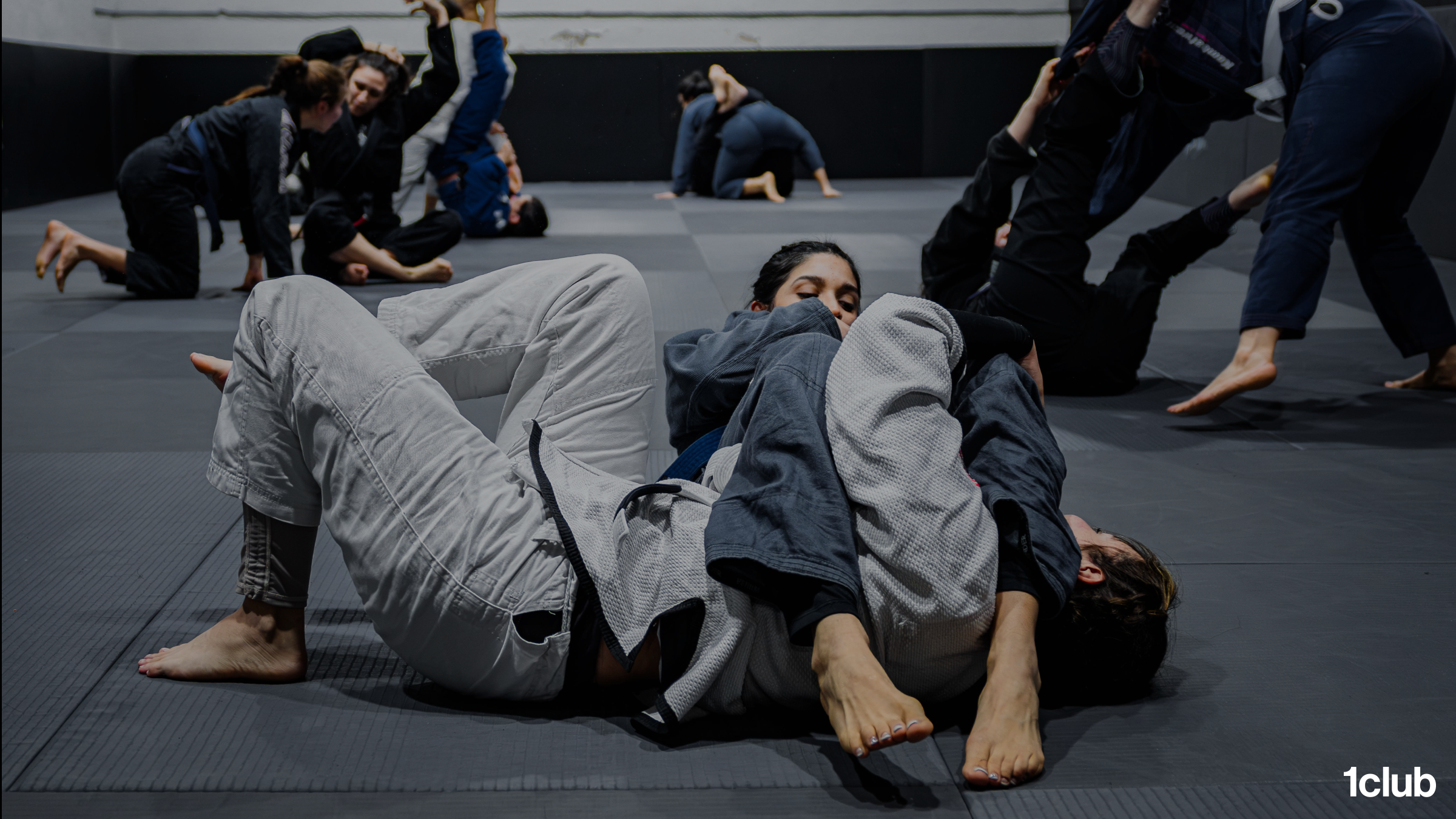 A full mat of adult students training in pairs during a jiu jitsu class