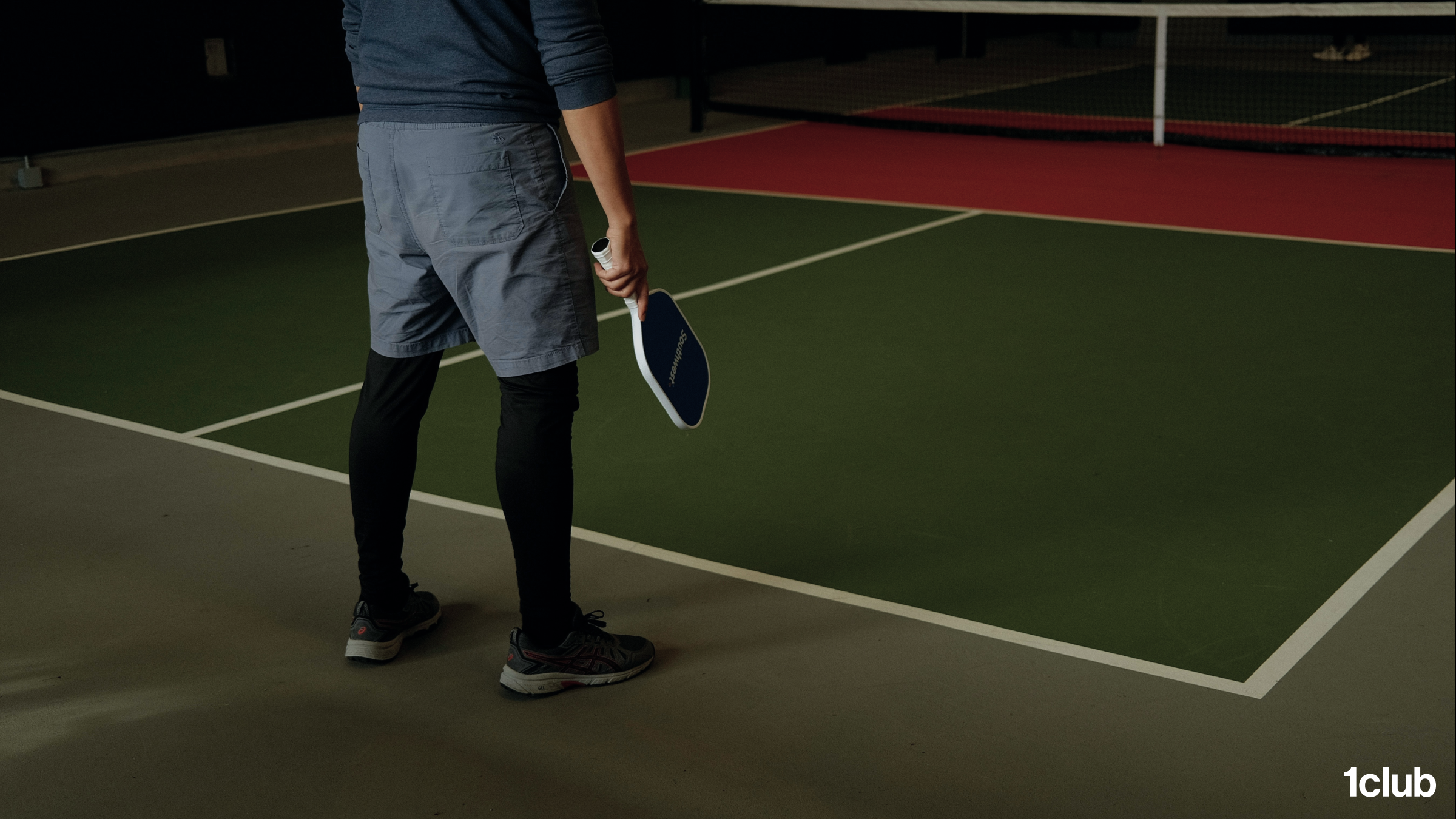 A single player waiting with a paddle on a quiet indoor pickleball court at a racket club