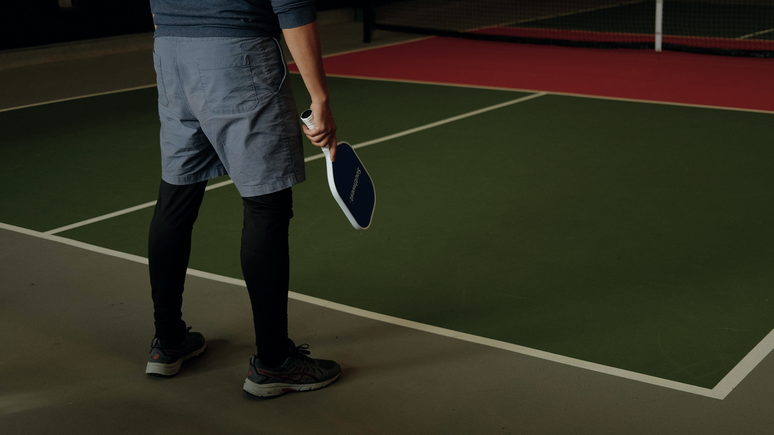 A single player waiting with a paddle on a quiet indoor pickleball court at a racket club